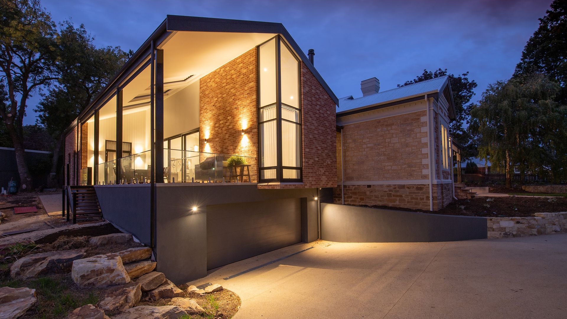 Modern glass house glowing at dusk among tall trees