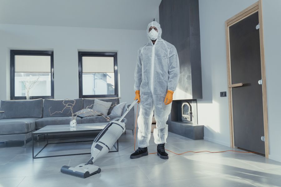 A cleaner in protective gear vacuuming an empty room