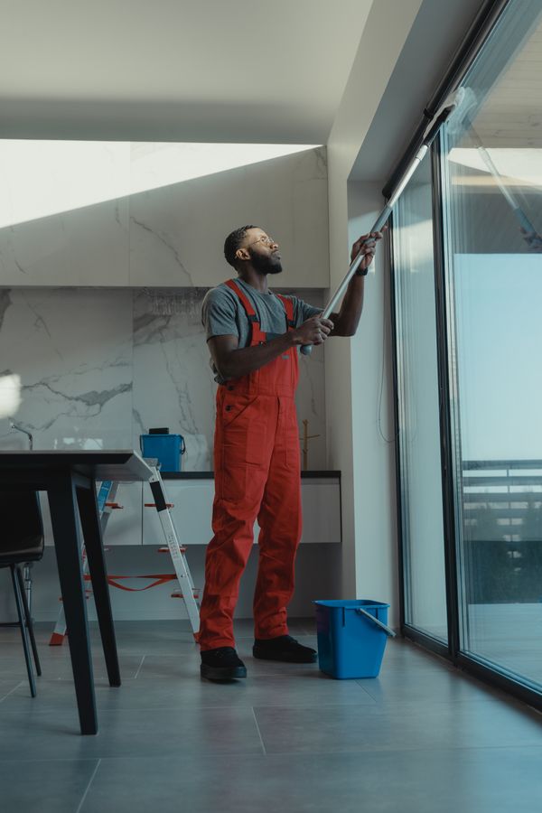 Cleaner wiping down a glass door in a bright home