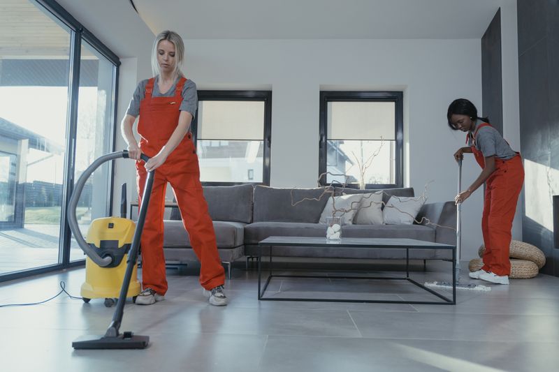 Two cleaners vacuuming and tidying a modern living room