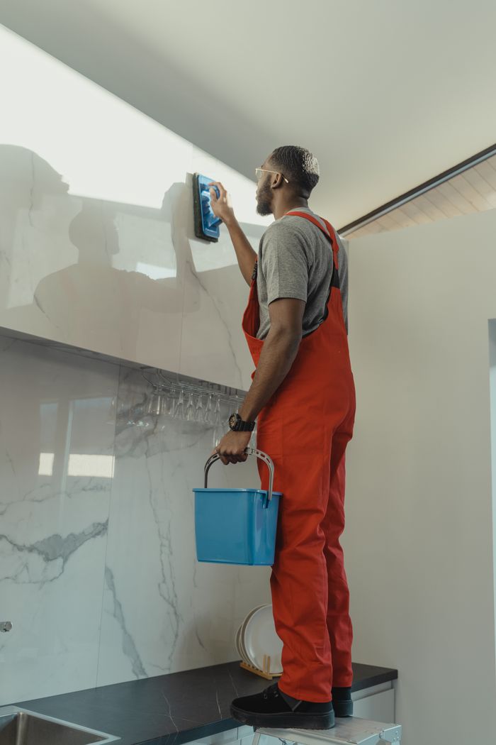 Cleaner scrubbing a kitchen wall with a brush
